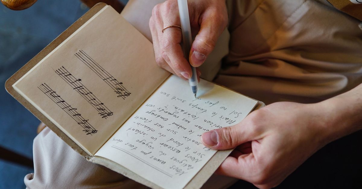 Male songwriter writes lyrics and music notes in a notebook, capturing the creative process.